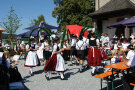 Kinder in Tracht tanzen in der Mitte von Zuschauern die auf Bierbänken sitzen