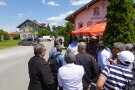 Ein Mann steht vor einem traditionellen Gasthaus in Bayern und erklärt etwas vor einer Gruppe mit einem Bild. 