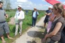 Eine Gruppe von Personen steht auf einem Feldweg und hört einem Sprecher aufmerksam zu.