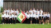 Ein Gruppenfoto von jungen Menschen mit weißer Bluse und schwarzem Rock und Vereinsfahne.