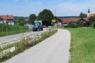 Traktor auf einer Straße, die einen Blühstreifen und einen Radweg hat