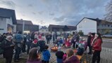 Mehrere Menschen, darunter viele Kinder, stehen vor einem Lagerfeuer.