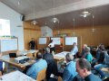 Ein Bild von einem Saal mit vielen Teilnehmern auf Stühle, vorne steht eine Frau, die etwas präsentiert.