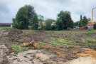 Kraterähnliche Landschaft mit aufgewühlter Schlamm-Erde. Kleine Baumstümpfe. Im Hintergrund Baumaschinen.