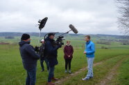 Zwei Personen stehen vor einer ländlichen Kulisse, drum herum ein Fernsehinterteam.