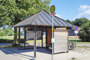 Ein Holzpavillon, rechts davon eine Bushaltestelle
