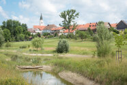 Ein Weiher vor einem Dorf mit Kirche.