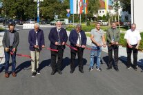 Mehere Personen stehen auf einer Straße und schneiden ein Band zu Einweihung durch.