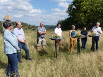 Mehrere Menschen stehen in einem Kreis auf einem Feld und sprechen miteinander.