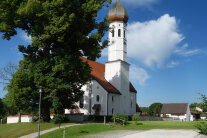 Kirche mit Kirchturm vor weiß-blauem Himmel.