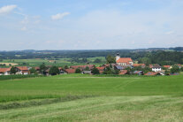 Das Dorf Ainring vor einer bewaldeten Bergkulisse