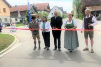 Mehrere Personen stehen auf einer Straße und schneiden ein Band zur Eröffnung durch.