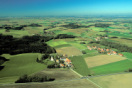 Landschaftsaufnahme aus der Vogelperspektive. Wiesen, Felder, Wälder und zahlreiche Ortschaften. Am linken Horizont der Flughafen München.