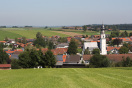 Blick auf ein Dorf mit markantem Kirchturm in einer kleinen Senke