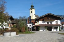 Der neugestaltete Schlechinger Dorfplatz mit Brunnen und Rathaus, der Kirchturm erhebt sich dahinter.